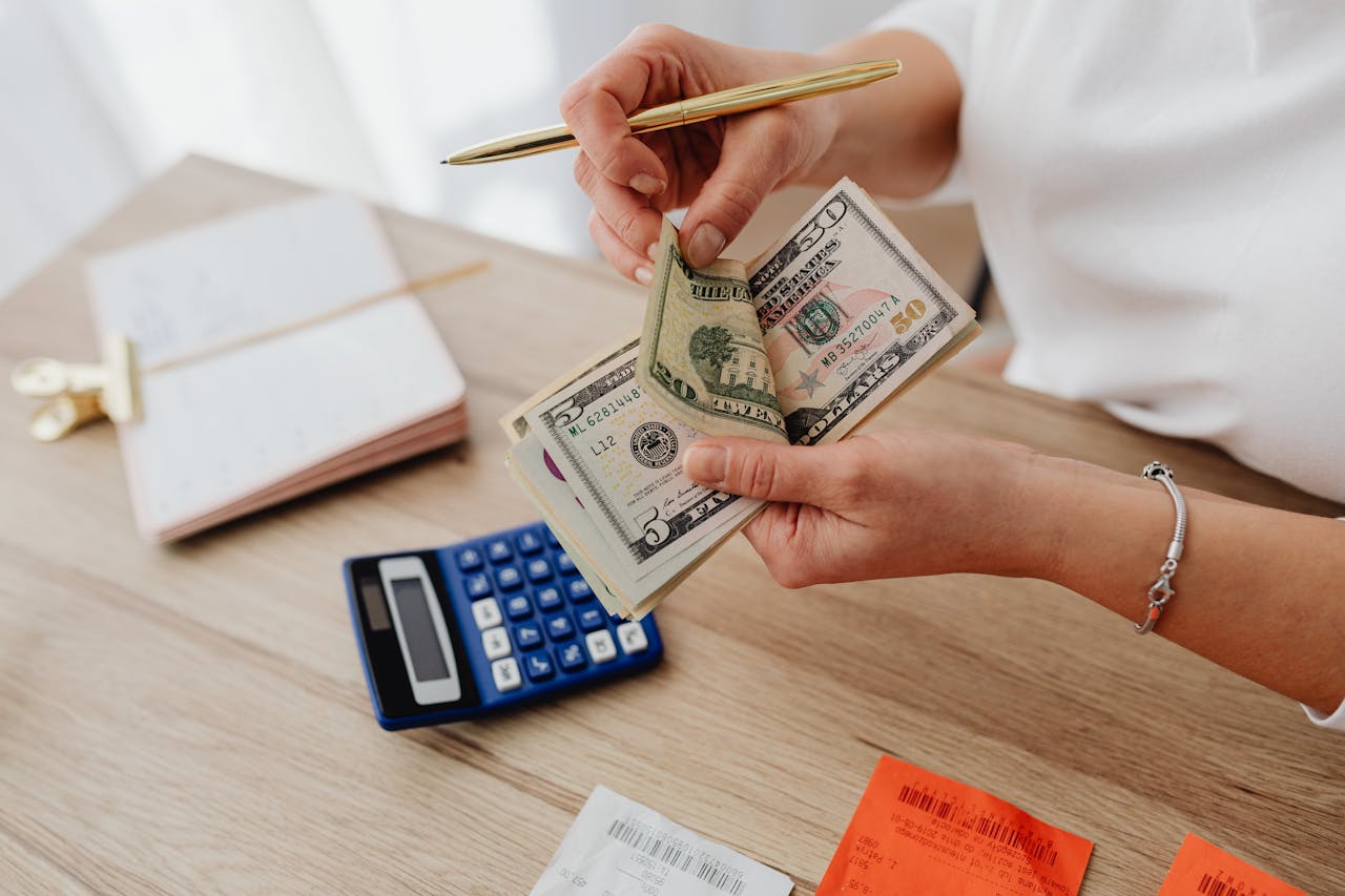 Woman counting cash with a calculator at a desk, managing finances.